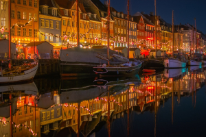 Night view of a cityscape in Denmark with illuminated buildings and reflections on water.